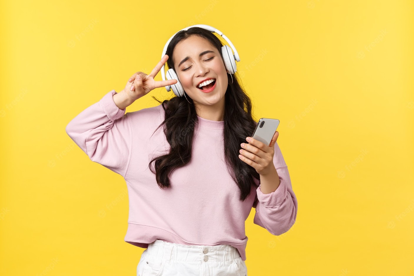 Imagem de uma mulher feliz, escutando música com fones de ouvido, ela veste uma blusa cor de rosa, e seu cabelo tem cor castanha